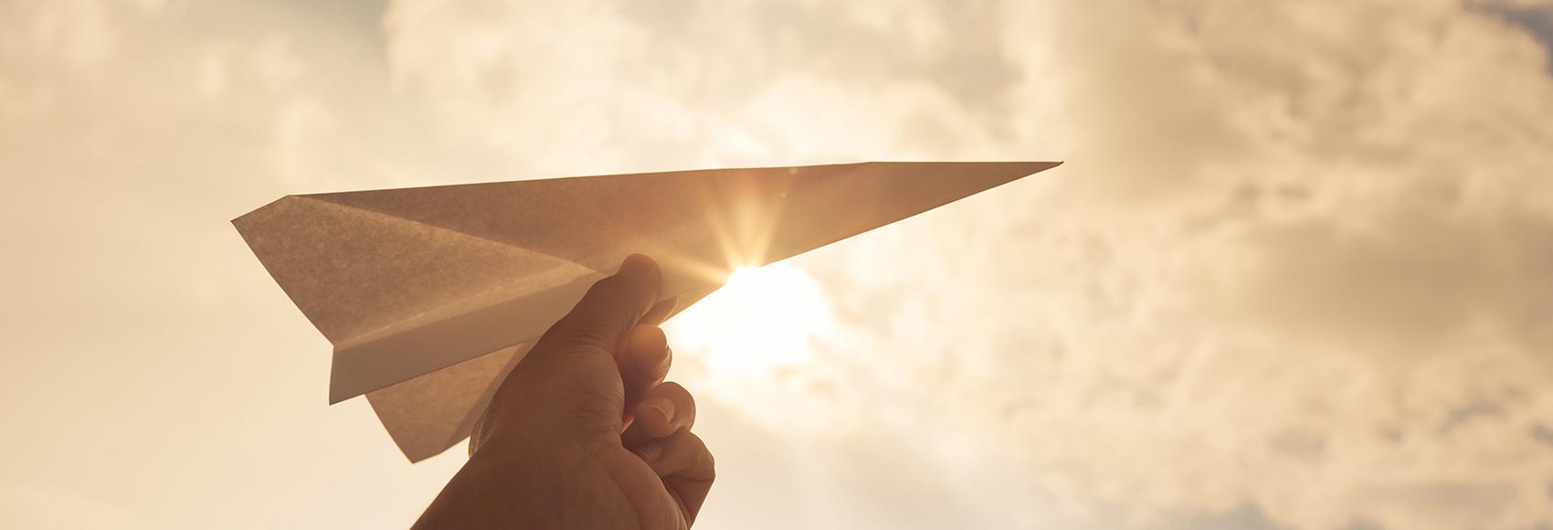 Main tenant un avion en papier dans le ciel