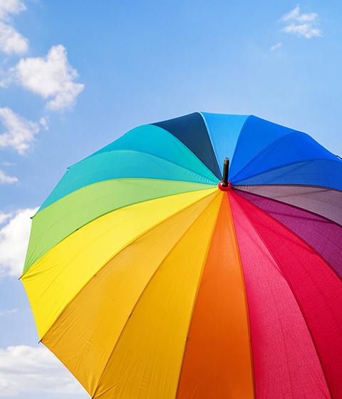 Rainbow colored umbrella against blue cloudy sky