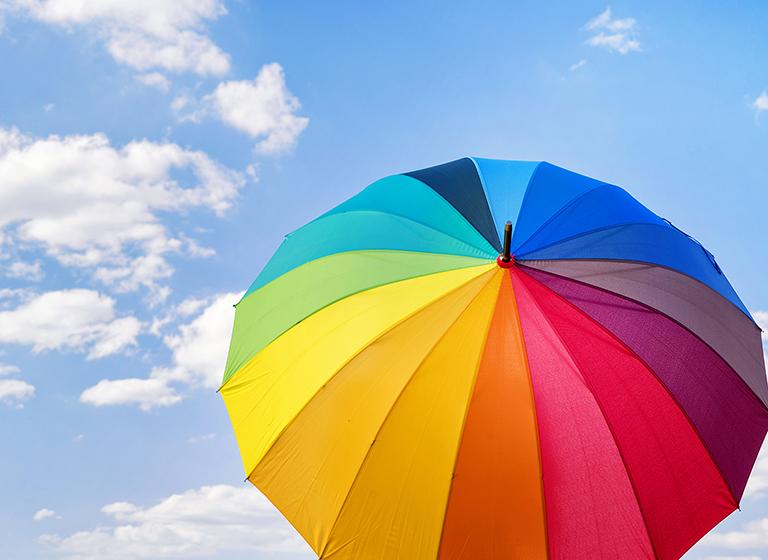 Rainbow colored umbrella against blue cloudy sky