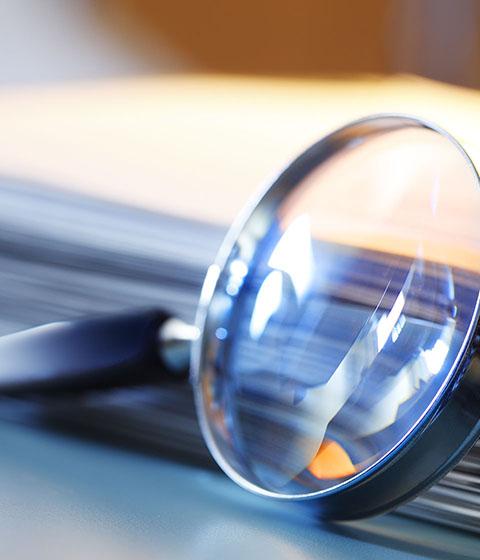 A magnifying glass leans against a thick stack of papers